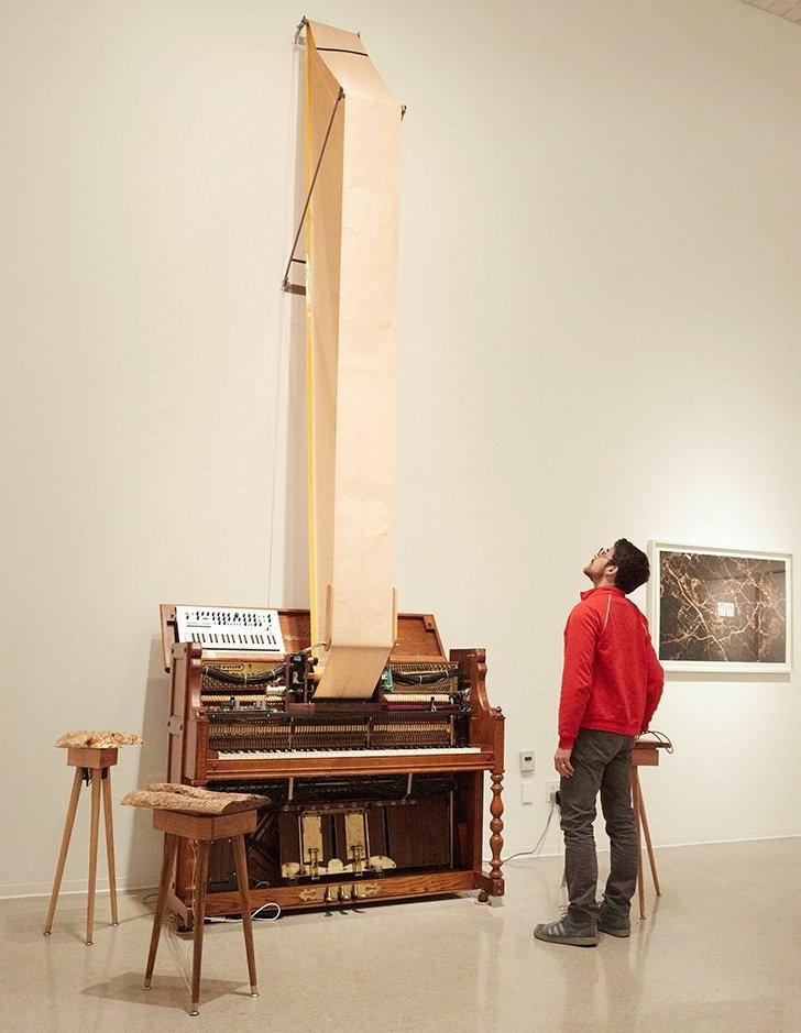 student looks at an art piece consisting of a piano and a long piece of sheet music